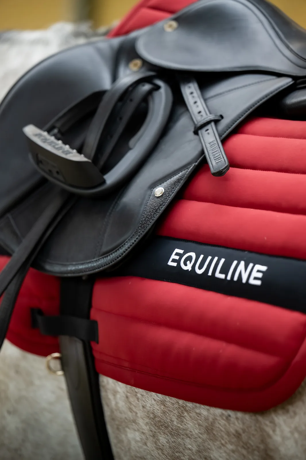 Close-up of the red Equiline EQCRISCE saddle pad with its black EQUILINE band under a black saddle.