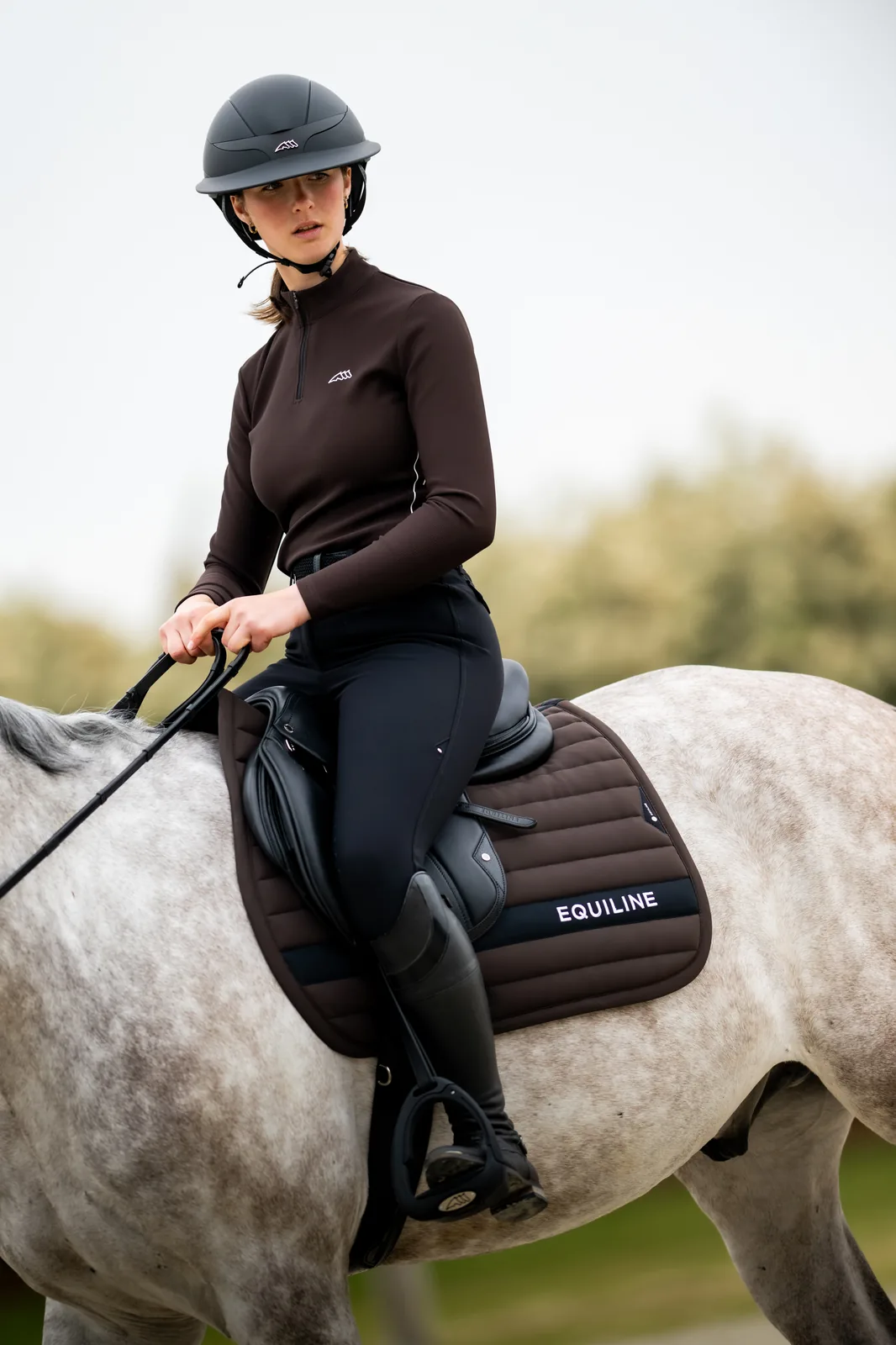 Rider in the brown Equiline EQEBLE technical top on a grey horse with the brown EQCRISCE saddle pad.
