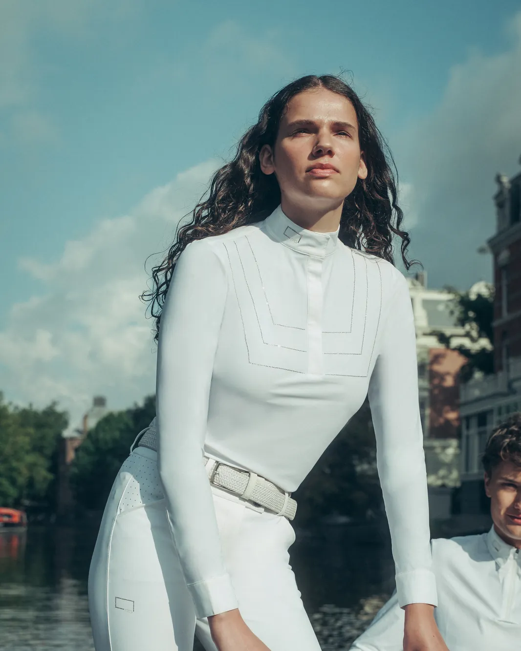 Rider at the helm of a boat in Amsterdam wearing a white show shirt, a braided belt and the RG white high-waisted riding breeches.